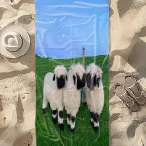 A towel with three black-faced sheep standing on green grass under a blue sky.