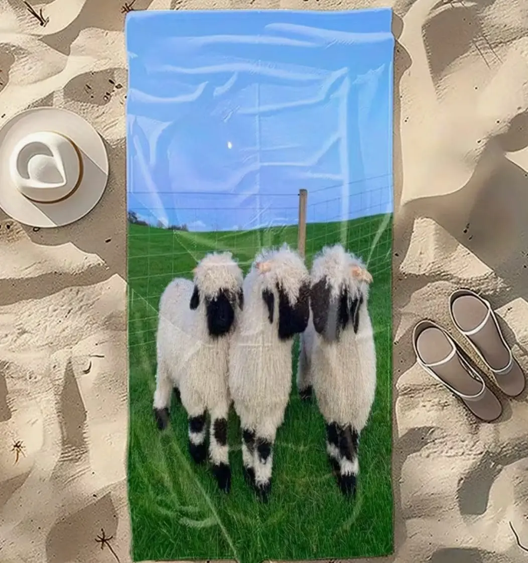 A towel with three black-faced sheep standing on green grass under a blue sky.