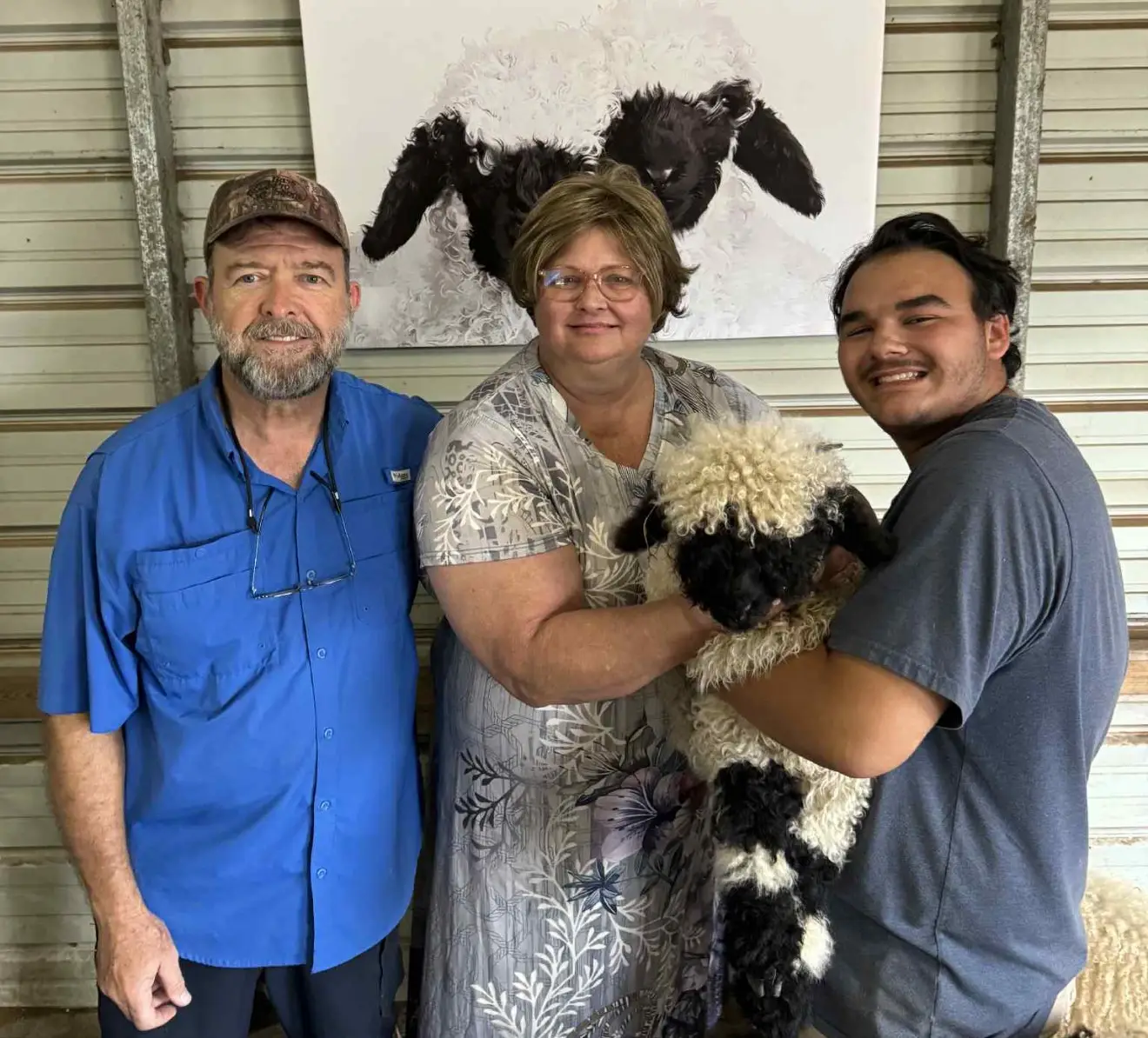 Three people smiling with a black and white dog indoors.